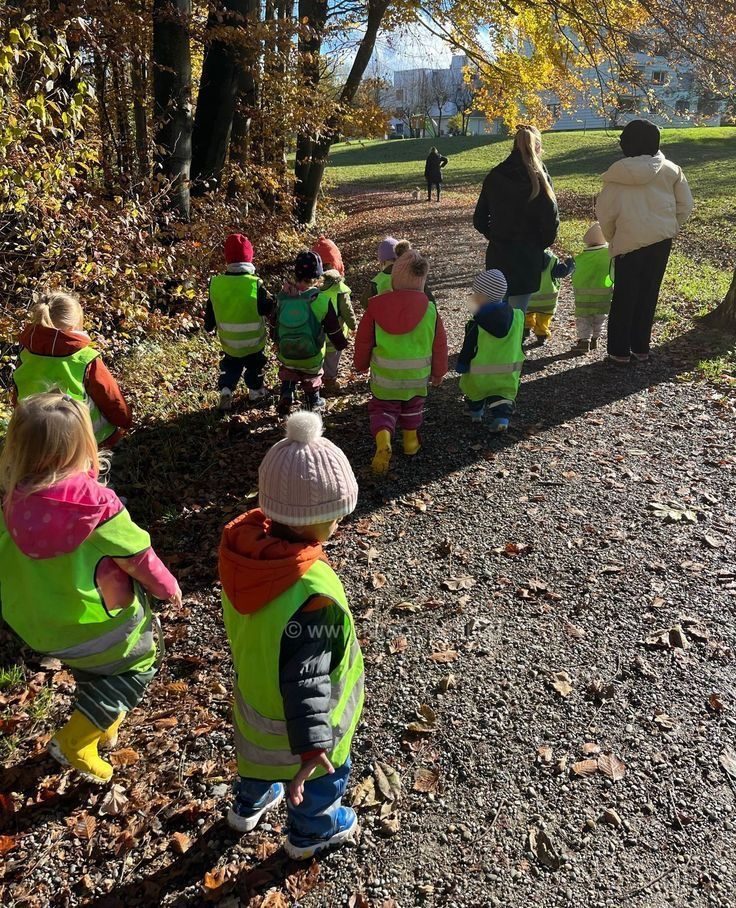 Förskolebarn i reflexvästar går på en skogspromenad med pedagoger