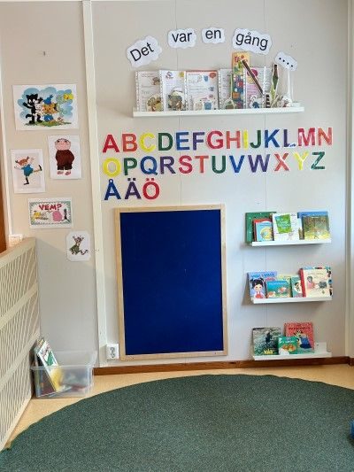 Läshörna på förskolan med bokhyllor, alfabet på väggen och grön matta